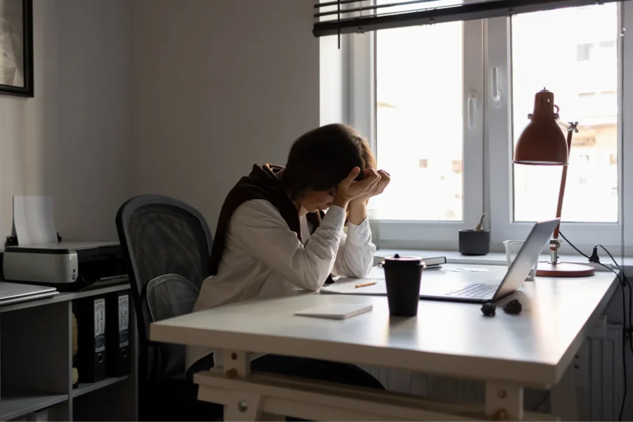 Une femme assise à son bureau pose sont front dans ses mains pour tenter de calmer son stress au travail